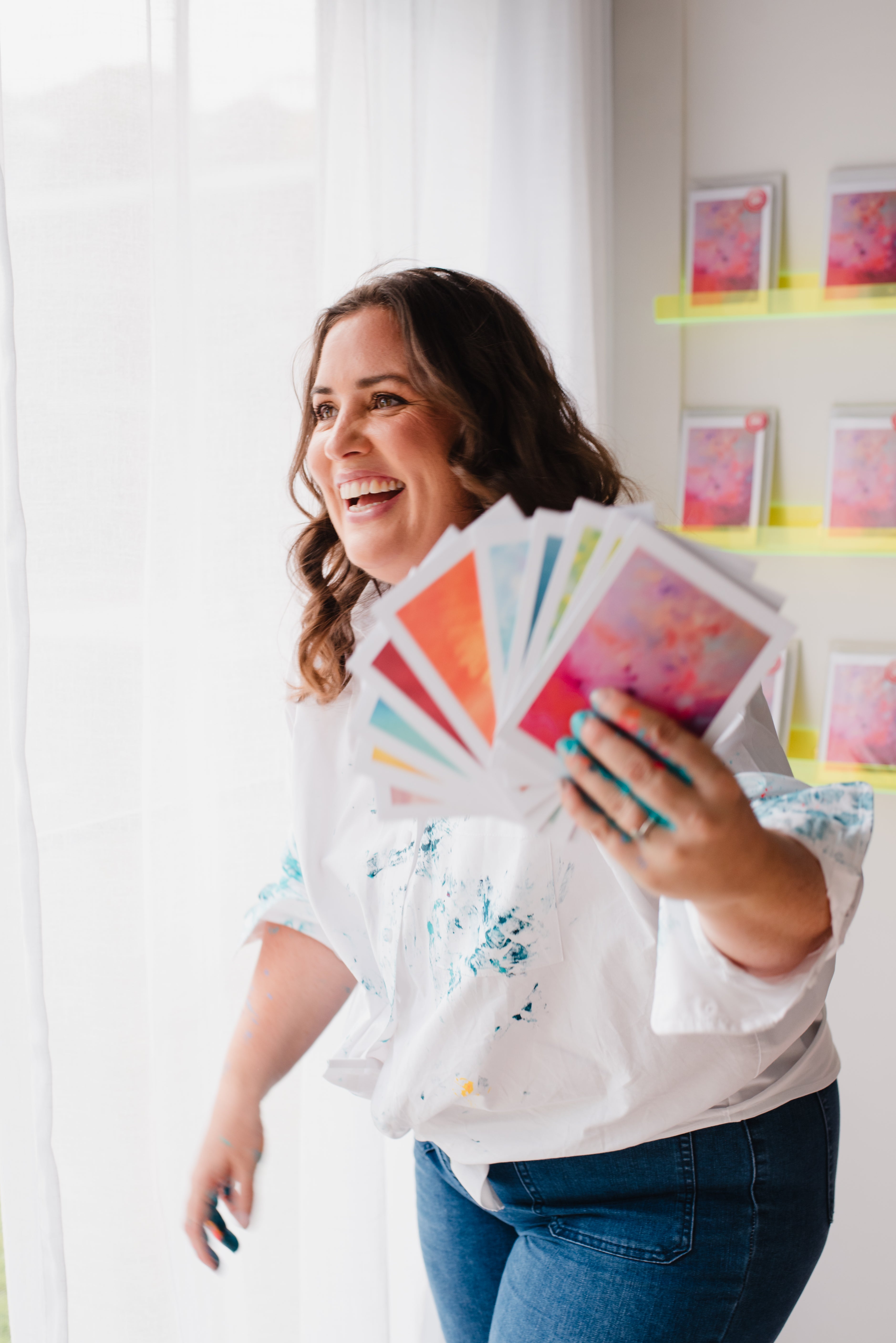 Woman holding colourful cards in a bright room with art on the wall.